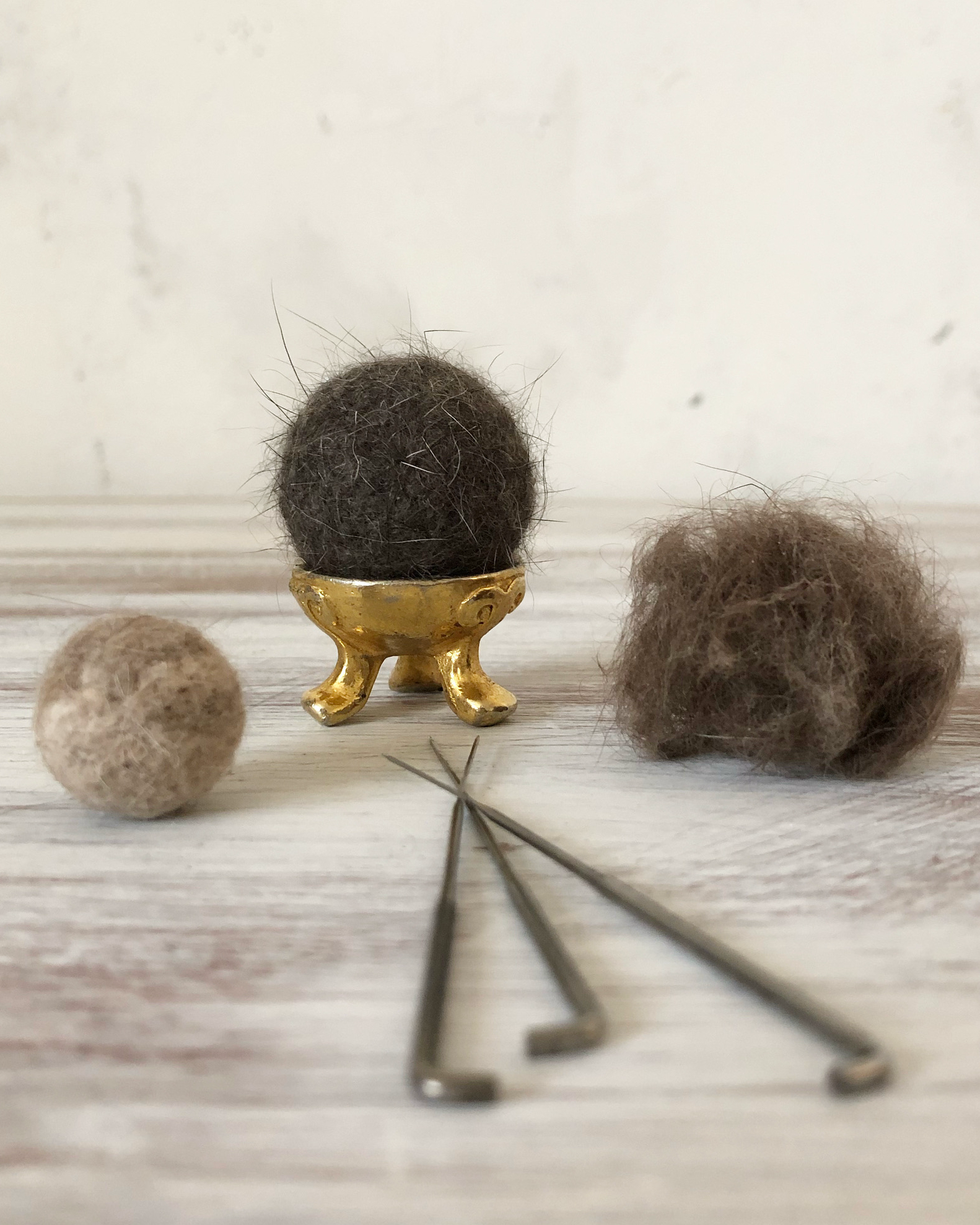 Three felted hair balls with needles in the foreground